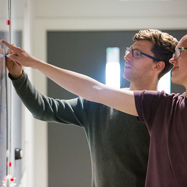 Students pointing together at a whiteboard