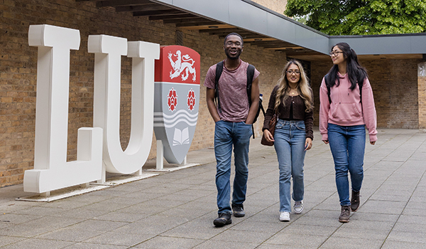 Three students walk past a giant LU sign on campus