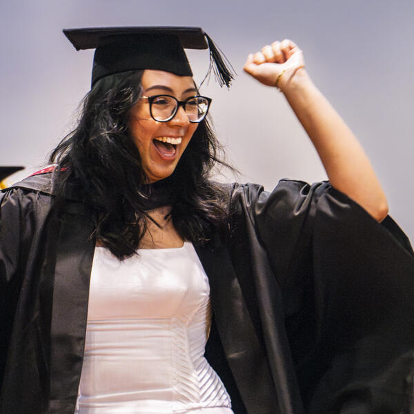 A student raises an arm in celebration at a graduation ceremony.