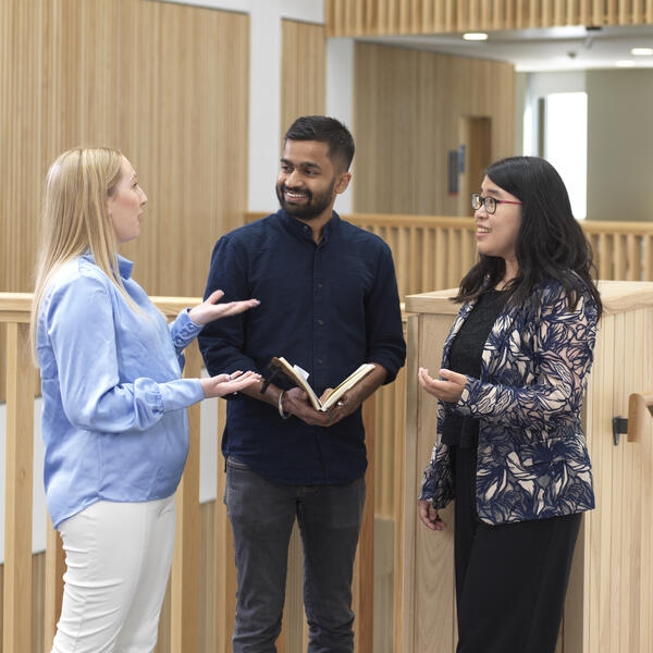 Three people talk whilst standing in a modern wood-paneled office.