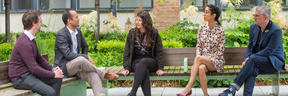 Five members of staff sitting on a bench and having a conversation.