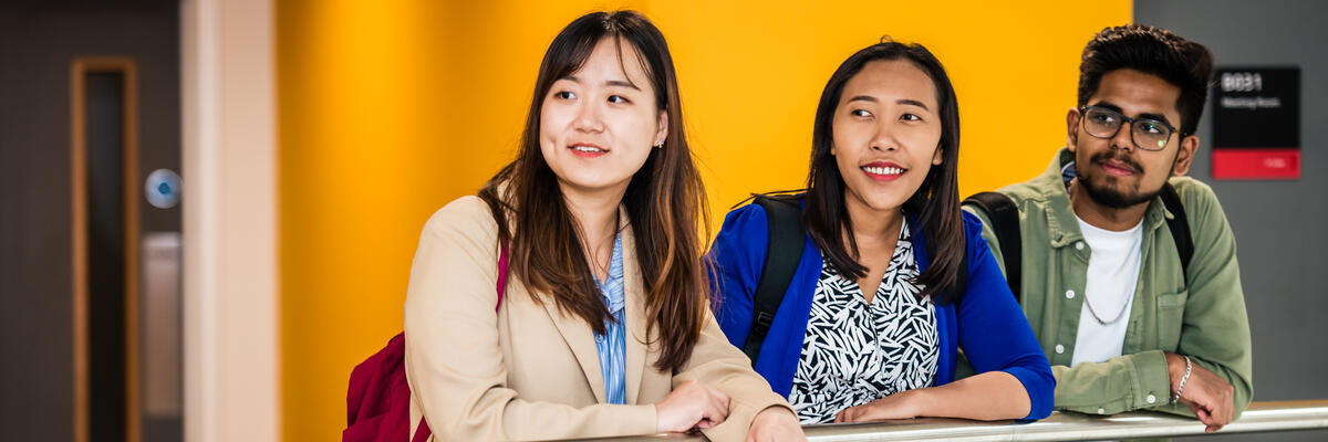 Three students lean over a bannister.
