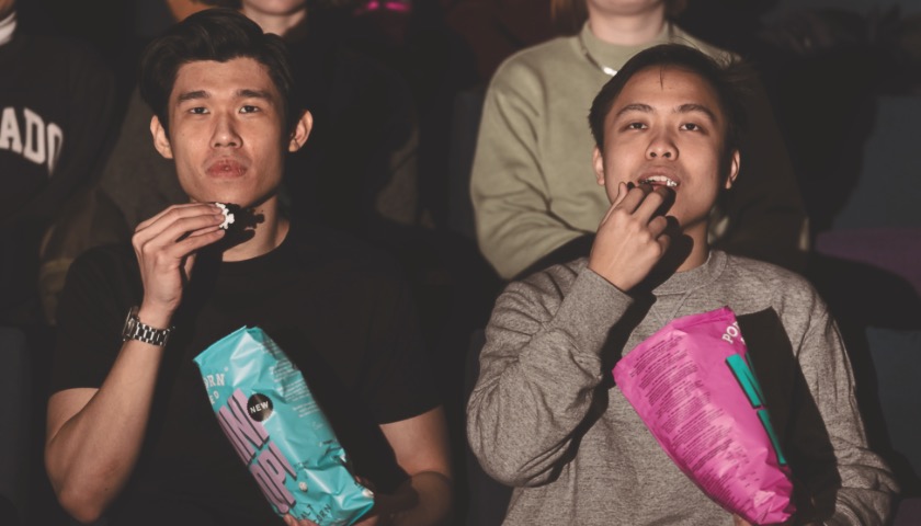 Two students sit in a darkened cinema eating popcorn