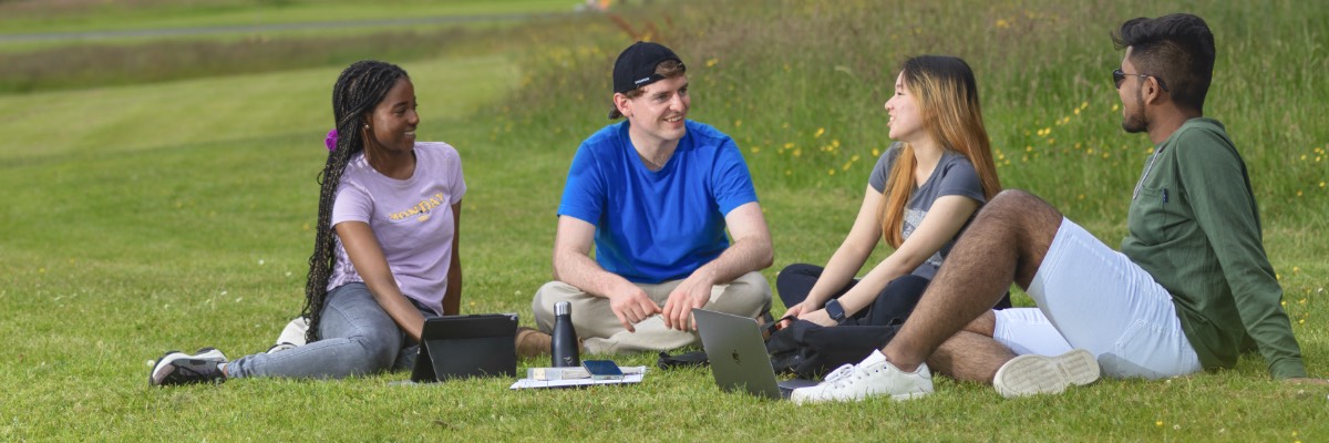 Four students sat on the grass over looking the grounds.
