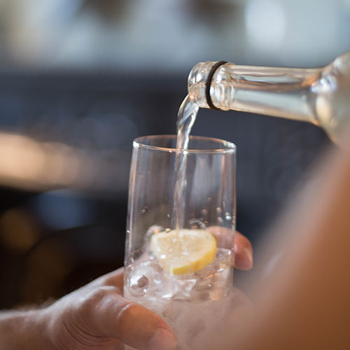 A bottle of water is poured into a glass on top of the lemon.