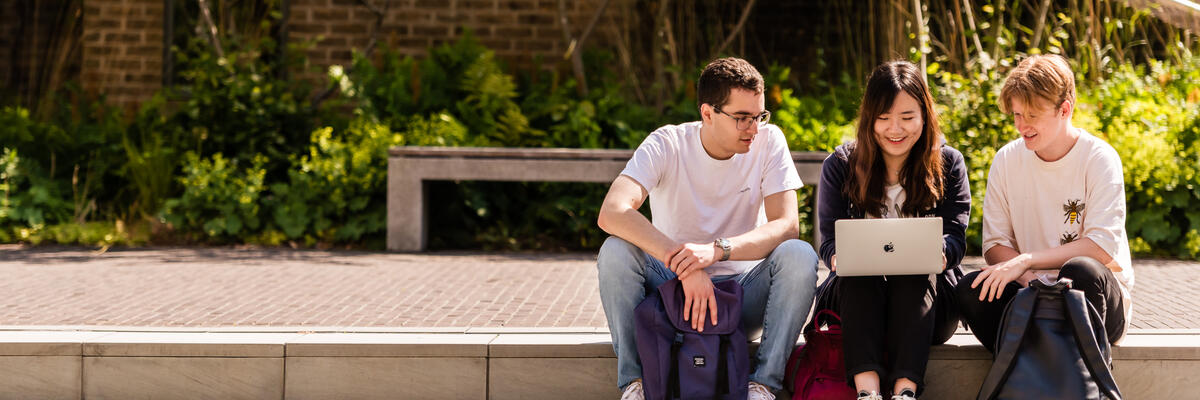 Students sitting around a laptop outside