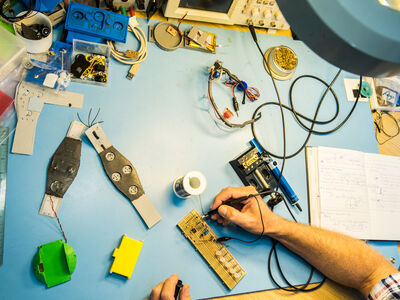 A soldering station, soldering ion and a person working on a circuit board and component