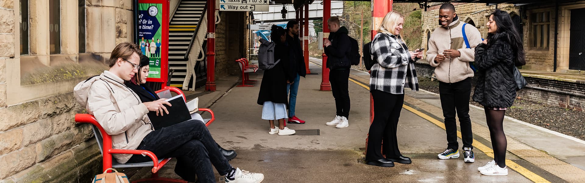 Students in Lancaster Train Station with bags on, waiting for a train