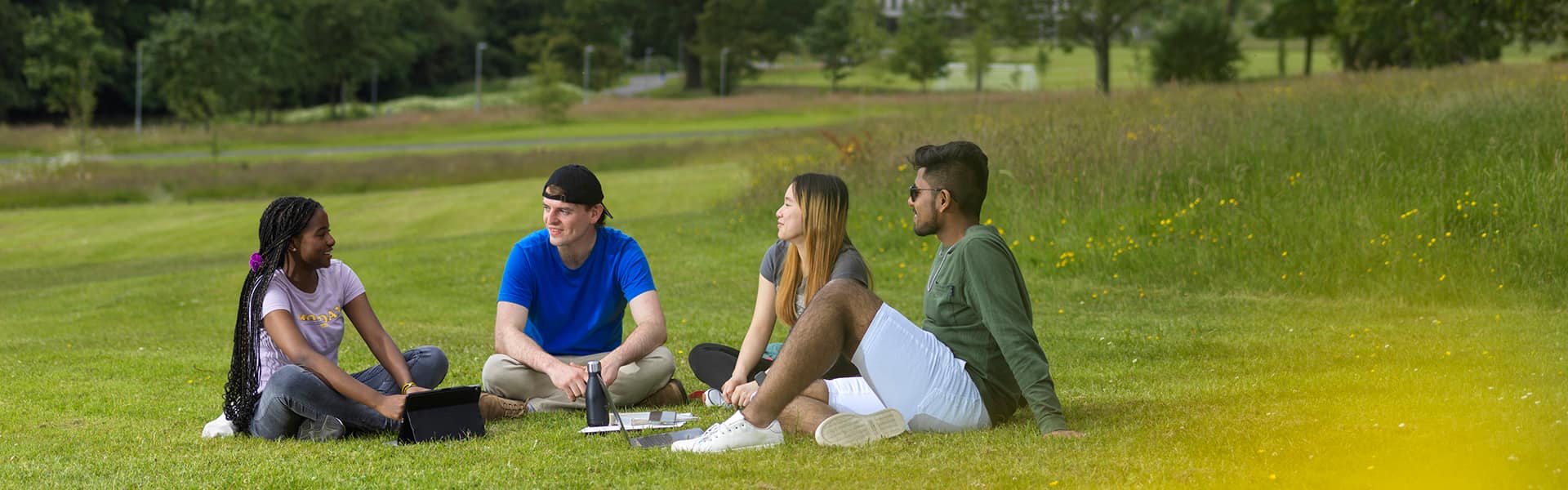 Students sat on the grass smiling with a sunny background